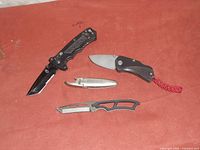 Four pocket tools including folding knives and multi-tools on a red surface