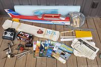 Lot layout showing partial RC airplane fuselage and tail, boxed starter, remote control, engines, blueprints, magazines, and miscellaneous parts.