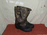 Pair of men's Absolute Zero winter boots in Mossy Oak camo pattern with black lower section and adjustable strap.