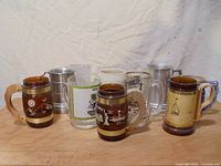 Group photo of 11 vintage beer steins and mugs, showing variety in materials and designs.