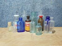 Overall arrangement of 11 vintage glass medicine bottles in assorted colors and sizes against blue textured backdrop