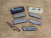 Full view of six harmonicas and two storage cases arranged on a wooden surface.
