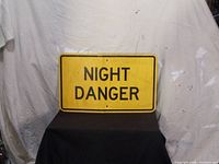 Front view of vintage yellow road sign with black text 'NIGHT DANGER'.