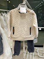 Front view of cream knit sweatshirt with button shoulder detail and matching navy pants displayed on hanger