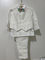 Full frontal image of the 4-piece white formal suit set for baby, showing shirt, vest, pants, and bow tie hung on branded hanger against plain background.