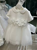 Front view of white baby dress showing Peter Pan collar, cap sleeves, and tulle skirt with floral and feather waist embellishments