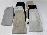Seven pairs of boys casual pants in various light and dark colors showing original tags on some pants.