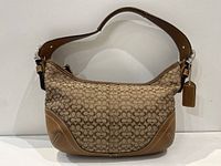 Front view of the small brown Coach bag showing signature 'C' pattern and leather trim on corners