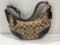 Front view of small Coach bag showing signature C logo canvas and dark leather accents with visible white stitching and gold-tone hardware.