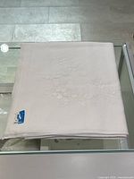Folded tablecloth showing embroidered floral motif and brand label