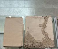 Photo of beige linen and cotton blend tablecloth folded, showing detailed beige lace edges with floral embroidery.