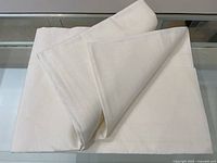 Folded large cream-colored linen flat sheet laid on display table.