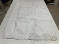 Photo of the folded white cotton bedspread showing lace fringe edge detail.