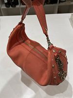 Side angle view showing leather texture, metal chain accents, and zipper on the handbag.