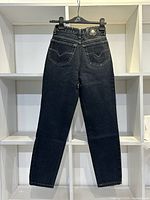 Back view of black Versace Couture jeans size 24 hanging, highlighting the two back pockets with V stitching and Versace branded button on waistband.