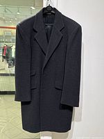 Front view of vintage men's charcoal wool coat hanging on hanger, showing notch lapel, flap pockets, and buttoned cuffs.