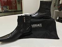 Pair of boots displayed on white surface with Versace Jeans Couture dust bag visible