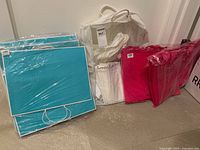 Photo showing turquoise paper bags stacked and shrink wrapped, pink paper bags in plastic, and white plastic bags of different sizes.