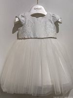 Front view of the white baby dress on a hanger showing lace bodice and full tulle skirt