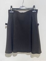 Front view of black A-line skirt hanging on black hanger, showing the flared shape and bow details on sides.