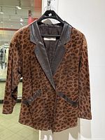 Front view of leopard print suede jacket with leather lapels and pocket accents hanging on a hanger.