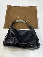 Photo of the black patent canvas Gucci handbag with the brown Gucci cloth storage bag behind it.