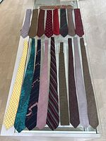 Lot of 18 vintage skinny ties laid out on table, showing a variety of colors and patterns including solids, stripes, polka dots, and abstracts in silk and wool fabrics.