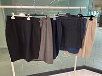 Seven women's skirts hanging on a rack, showing different colors and styles including black, gray, navy, denim, and beige skirts.