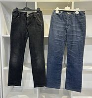 Front view of two pairs of women's vintage Versace jeans hanging side by side, one black and one blue pair, showing front pocket and button details.