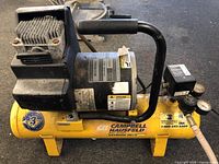Front view of yellow Campbell Hausfeld air compressor with model and serial number visible on the motor label and manufacturer stickers on the tank.