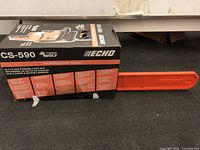 Chainsaw in original box with orange protective bar cover visible