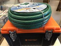 Green light duty garden hose coiled and strapped on top of the orange black Tactix toolbox.
