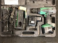Top-down photo showing the full Hitachi cordless drill set in its carrying case, including the cordless drill, two batteries, charger, and case compartments.