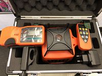 Photo of the laser level kit inside a foam-padded metal case showing the rotary laser level, remote, receiver, and charger.