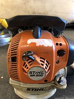 Close-up of orange Stihl SR 200 gas engine showing the pull-start and control features.