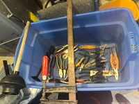 Photo of blue bin containing assorted pliers, wrenches, snippers, and clamps with a hand plunger placed next to the bin.
