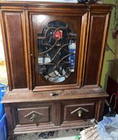 Front view of the antique wooden hutch showing glass door with wooden lattice, side panels, and two bottom drawers with brass knobs.