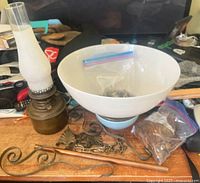 Overall lot showing antique oil lamp components including glass chimney, brass base, large white bowl, chains, and bag of decorations.