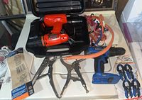 Cordless drill in case alongside clamps, bungee cords, wrench, locking pliers, and sandpaper