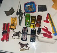 Top-down photo of all items in the lot on a white surface showing toy cars, horse figurines, badges, plastic figures, lighter, and knives