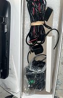 Close-up of cables bundled with rubber band and other accessories in plastic bag next to mirror dash cam.