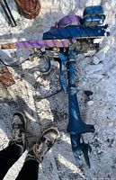 Outboard motor engine overview showing blue body and purple top cover with propeller attached at bottom, placed on snow-covered ground.