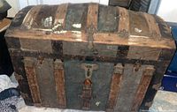 Front view of the antique steamer trunk showing weathered wooden slats and metal hardware with visible wear and patina.
