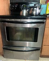 Front view of the stainless steel and black electric stove with oven closed, showing the digital control panel and viewing window on the oven door.