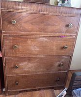 Front view of the tall boy dresser showing four drawers with brass knobs. Wood finish is faded with visible water marks and scratches.