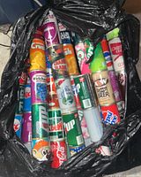 Full view of multiple vintage soda cans inside a black plastic bag, showing various brands and designs.