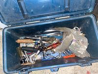 Open blue plastic toolbox showing assorted hand tools including screwdrivers, pliers, wrench, and metal bits inside, with a plastic bag and electrical cord