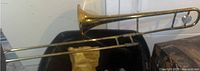 Full length view of the brass trombone lying on a surface, showing overall form and condition with visible dents.