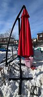 Closed red patio umbrella with black metal stand and base in snowy outdoor setting