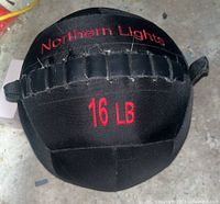 View of the front of the black Northern Lights exercise weight ball showing the 16 LB embroidered label and handles.